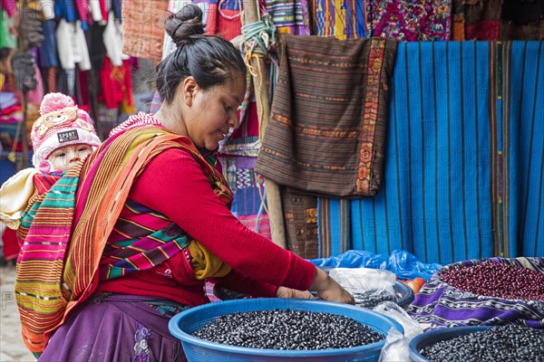 Local Mayan K'iche woman with child on her back selling beans on market day in the town Chichicastenango