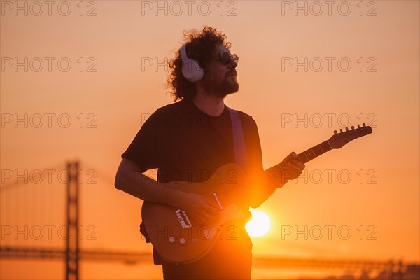 Hipster street musician in black playing electric guitar in street outdoors on sunset with lens flare and light leak