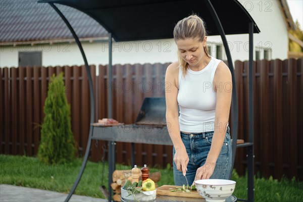 Cheerful woman makes vegetable salad on backyard