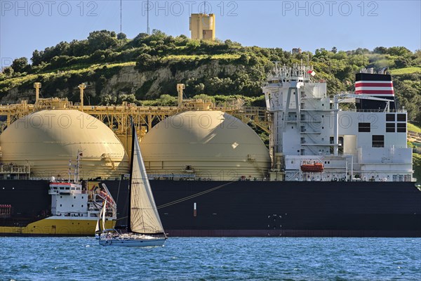 LNG or liquified natural gas tanker moored by industrial pier and green hill on sunny day. Alternative gas supply