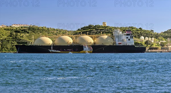 LNG or liquified natural gas tanker moored by industrial pier and green hill on sunny day. Alternative gas supply