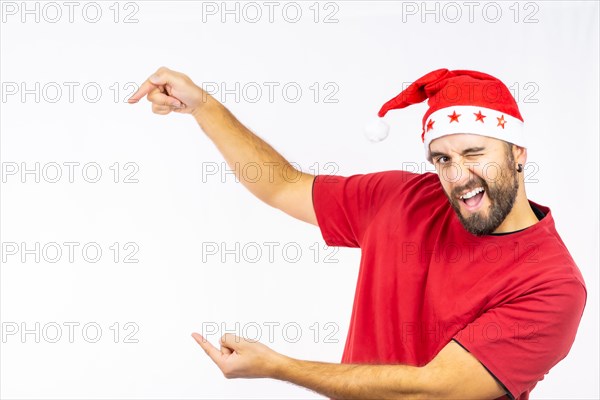 Young very happy Caucasian man with red Christmas hat pointing to the left on a white background