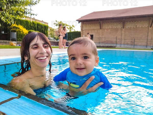 A young Caucasian mother with her baby enjoying the summer in their first swim in a swimming pool