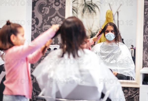 Client sitting by the mirror while waiting with her daughter. Reopening with security measures for hairdressers in the Covid-19 pandemic