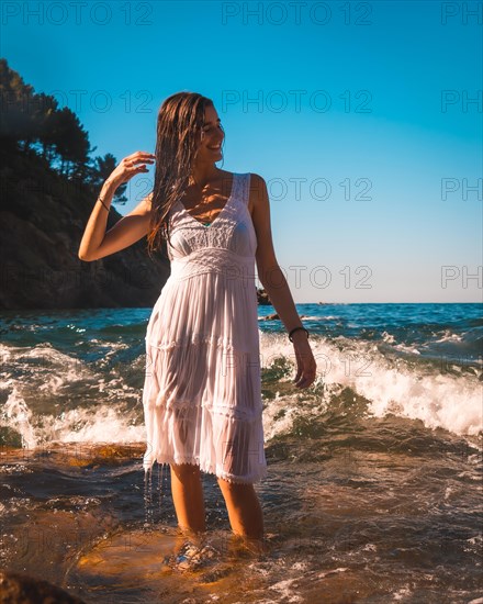 A young Caucasian brunette enjoying a bath in a white dress in the sea water