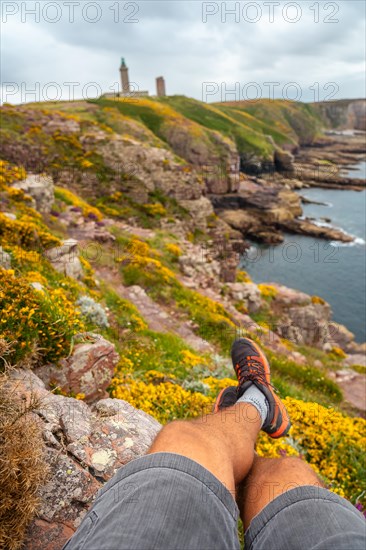 A young tourist sitting on the coast next to the Phare Du Cap Frehel