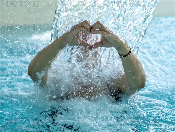 Woman Behind a Waterfall in a SPA Swimming Pool and Making a Heart Shape with Her Wet Hands in Switzerland