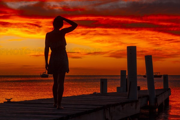 A young woman walking towards the Caribbean Sea in the orange sunset at the West End beach of Roatan. Honduras