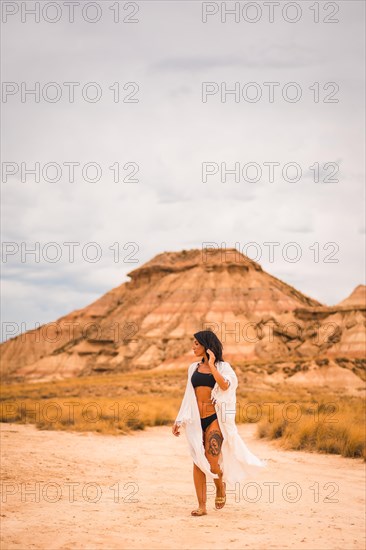 A young brunette Caucasian girl in a white dress walking barefoot through a desert