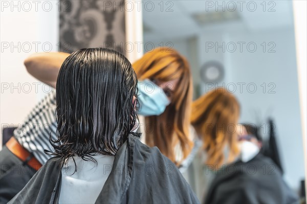 Young brunette girl with mask in a hairdresser cutting her hair. Reopening with security measures for hairdressers in the Covid-19 pandemic. New normal