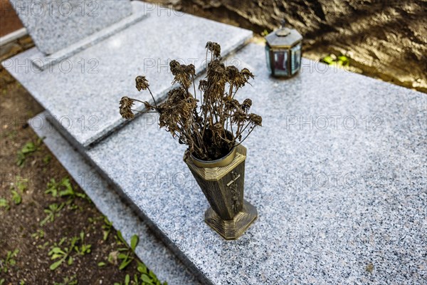 Vase with withered flowers on a grave in a cemetery