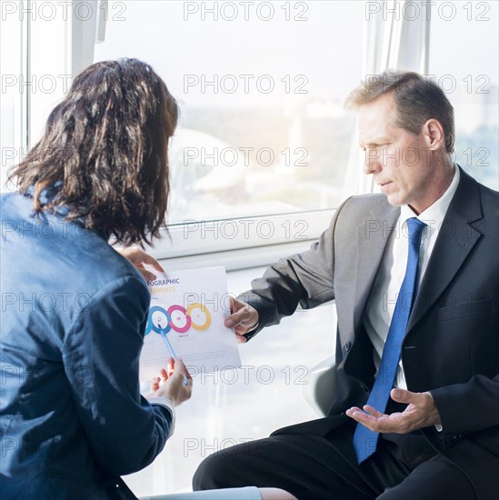 Businesswoman explaining infographic elements sheet her male partner