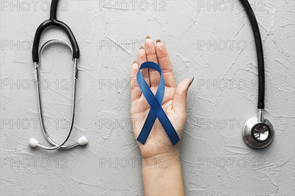 Crop hand with blue ribbon near stethoscope