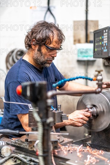 Worker in the metal industrial factory trade in the numerical control sector in CNC lathe processing