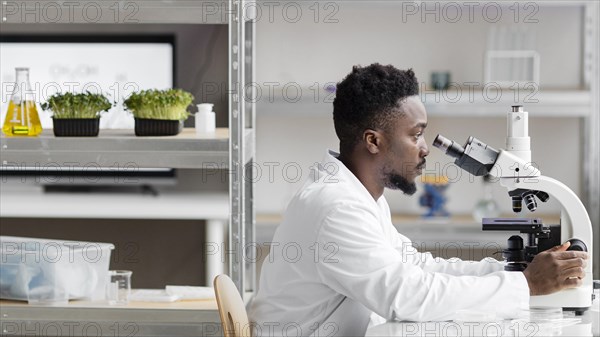 Side view male researcher laboratory looking through microscope