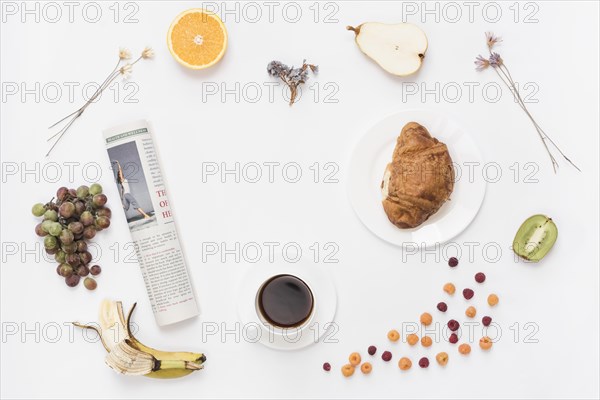 Rolled up newspaper with coffee cup croissant fruits white background