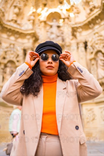 Fashionable latin woman with winter clothes and sunglasses posing next to an ancient monument