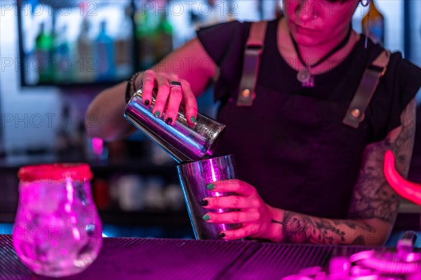 Close-up with focus on a female waiter mixing ingredient preparing a cocktail in the counter of a bar at night