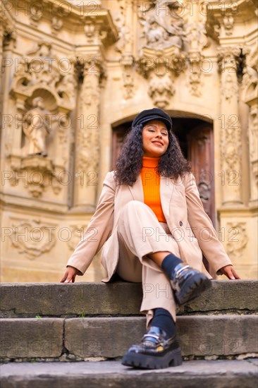 Vertical photo of a beauty latin woman posing with winter clothes sitting next to the entrance of an ancient Church