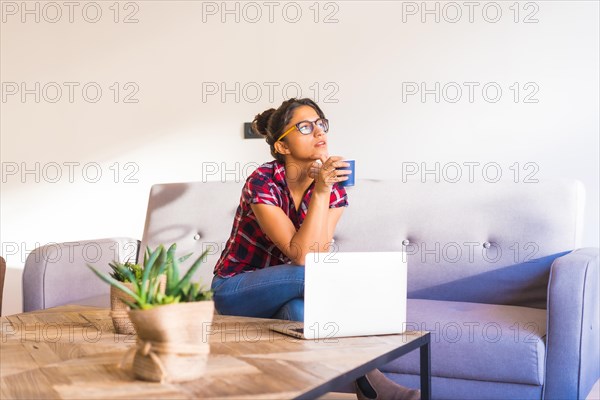 Horizontal photo with copy space of a pensive woman drinking coffee and using laptop at home