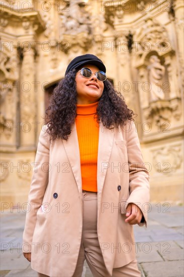 Stylish latin woman standing with warm elegant clothes in a square with an ancient monument