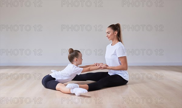 Beautiful female teacher helps a little girl stretch in a gymnastics class. The concept of education