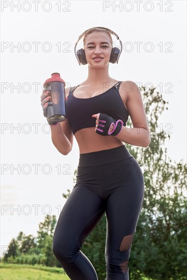 Girl posing with a sports nutrition shaker in the park. The concept of a healthy lifestyle. Sports Equipment. Fitness style advertisement. Mixed media