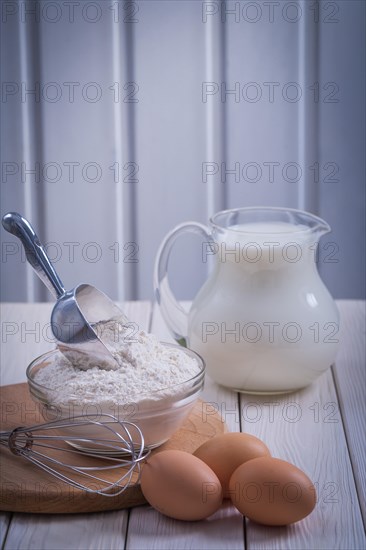 Corolla eggs flour bowl scoop jug milk on white lacquered old wooden board food and drink concept