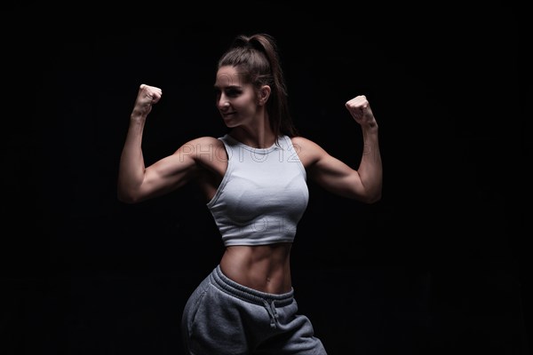 Athletic fitness woman posing in the studio on a dark background. Photo of an attractive woman in fashionable sportswear. Sports and healthy lifestyle. Mixed media