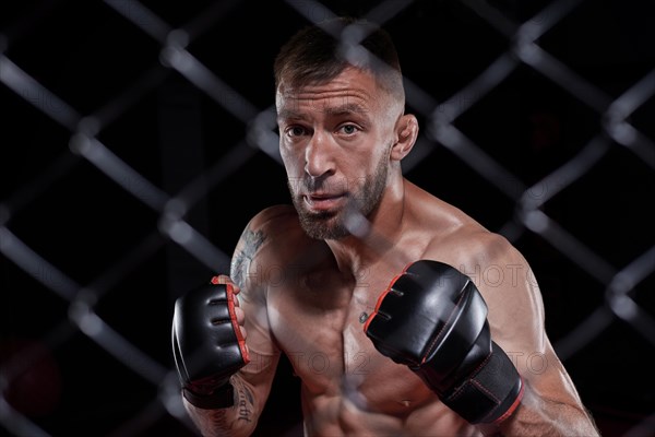 Dramatic image of a mixed martial arts fighter standing in an octagon cage. The concept of sports