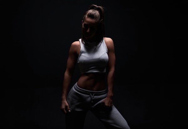 Athletic fitness woman posing in the studio on a dark background. Photo of an attractive woman in fashionable sportswear. Sports and healthy lifestyle. Mixed media