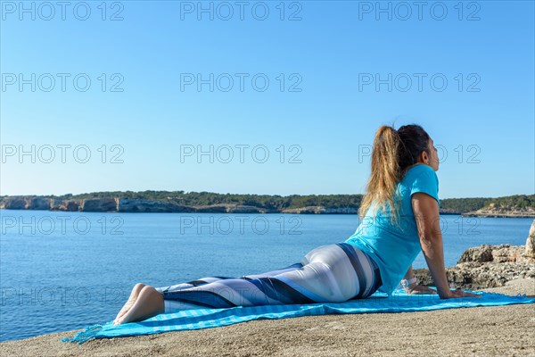 Middle-aged fitness woman outdoors in front of the sea does yoga stretching exercises