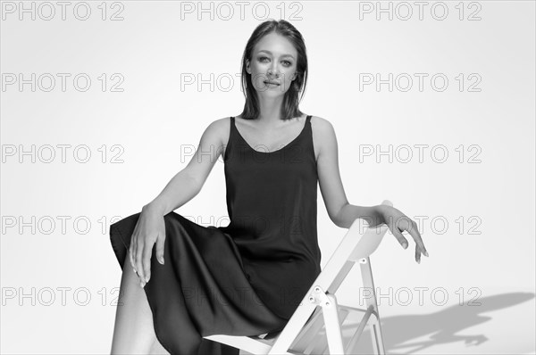 Beautiful girl posing on a white background sitting on a chair in a black peignoir. Underwear advertising concept.
