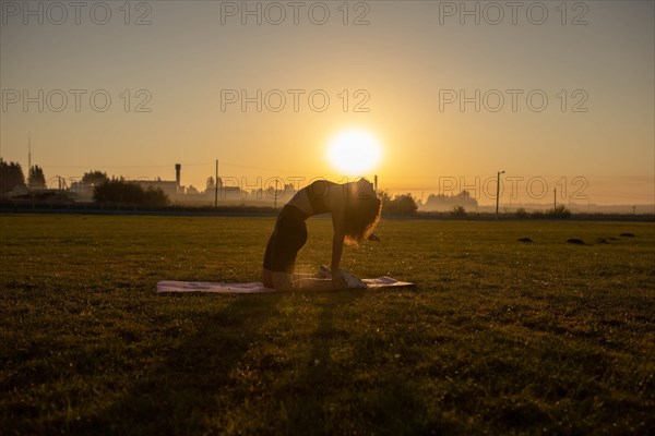 Young curly athletic girl in sportswear doing yoga on a yoga mat outdoors on the grass during sunset