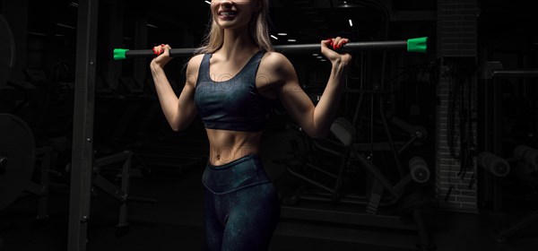 Charming blonde posing in the gym with a body-bar. Front view. The concept of sports