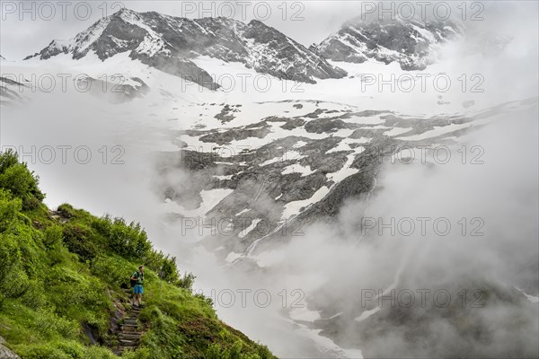 Mountaineers on a hiking trail, in the background glaciated peak Dosso Largo and glacier Schlegeiskees, cloudy atmospheric mountain landscape, ascent to Furtschaglhaus, Berliner Hoehenweg, Zillertal, Tyrol, Austria, Europe