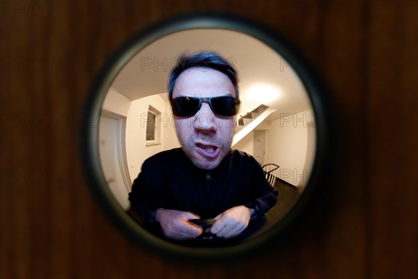 View through door viewer into a staircase, peephole, spyhole, with a man in front of the door, looking very angry, maybe landlord or bailiff