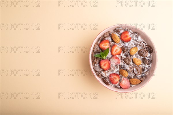 Chocolate cornflakes with milk, strawberry and almonds in ceramic bowl on pastel orange background. Top view, flat lay, copy space