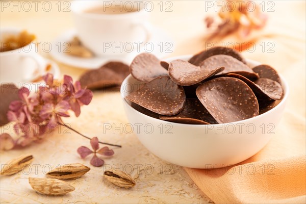 Chocolate chips with cup of coffee and caramel on a beige concrete background and orange textile. side view, close up, selective focus