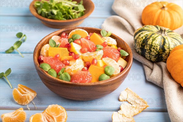 Vegetarian fruit salad of pumpkin, tangerine, pomegranate, grapefruit, sunflower microgreen sprouts on blue wooden background and linen textile. Side view, close up