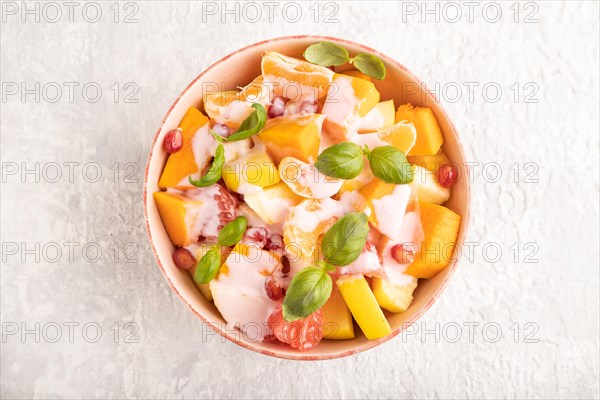 Vegetarian fruit salad of yogurt pumpkin, tangerine, pomegranate, grapefruit, basil microgreen sprouts on gray concrete background. Top view, flat lay, close up