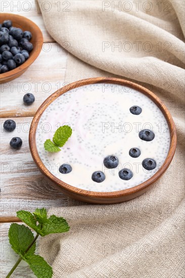 Yogurt with blueberry in wooden bowl on white wooden background and linen textile. Side view, close up
