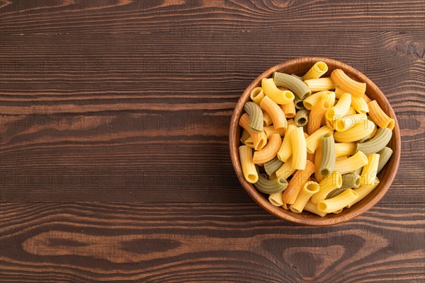 Rigatoni colored raw pasta with tomato, eggs, spices, herbs on brown wooden background. Top view, flat lay, copy space