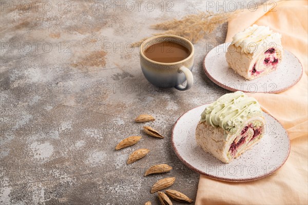 Roll biscuit cake with cream cheese and jam, cup of coffee on brown concrete background and orange linen textile. side view, copy space