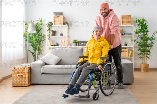 Portrait of a caregiver and a disabled man in wheelchair looking and smiling at camera at home