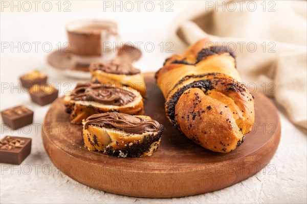Homemade sweet bun with chocolate cream and cup of coffee on a gray concrete background and linen textile. side view, close up, selective focus