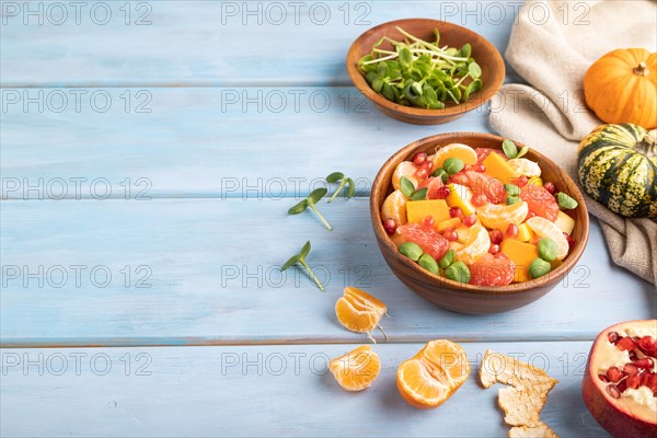 Vegetarian fruit salad of pumpkin, tangerine, pomegranate, grapefruit, sunflower microgreen sprouts on blue wooden background and linen textile. Side view, copy space
