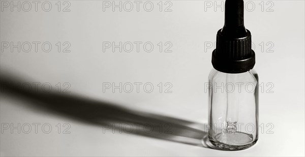 Closeup of single eye dropper bottle with strong dark shadow on white background