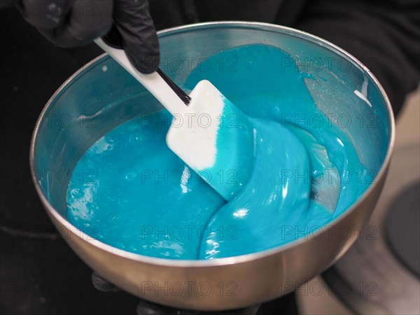 Sweet pastry chef stir a Bright blue icing being stirred with a spatula in a metal mixing bowl for as content for filling bag for cake decoration and dripping