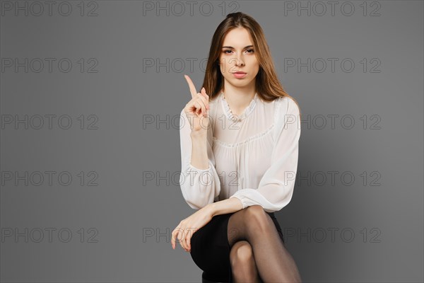 Strict young woman sitting on a chair with her index finger up